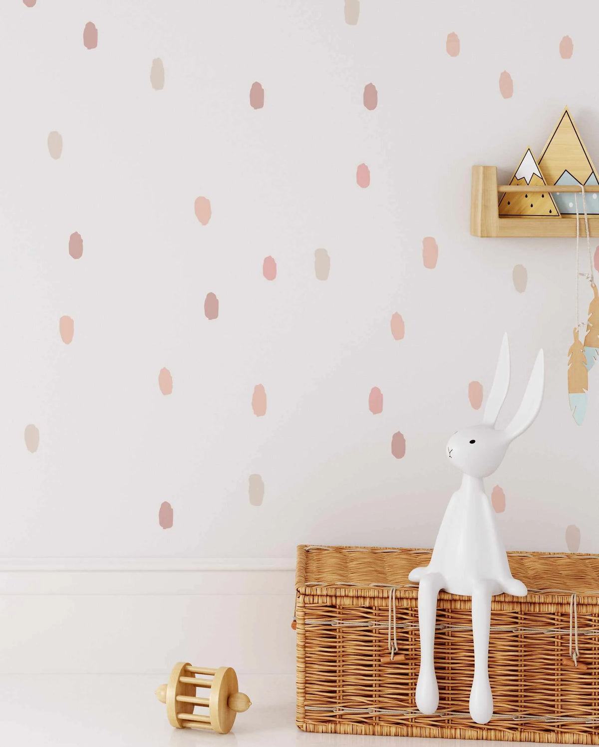 Nursery:
"White wall with a repeating pattern of hand-painted dots in various shades of blush pink, dusty rose, and pale beige. A white rabbit figurine sits atop a woven wicker basket in the foreground, with a wooden shelf holding mountain-shaped decor and feather garlands visible on the right."