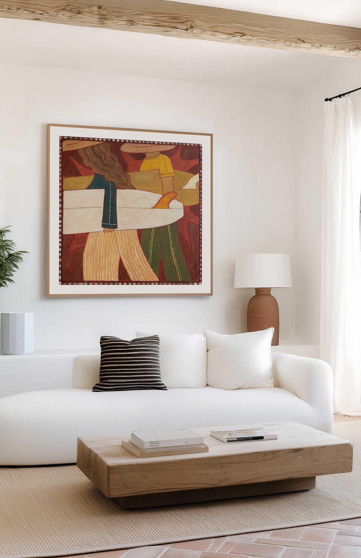 A framed abstract painting with warm earthy tones hangs on a white wall above a modern white sofa in a bright, contemporary living room with a wooden coffee table and natural light.