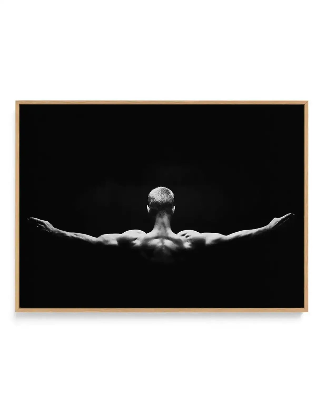 Black and white photograph of a muscular man viewed from behind with arms outstretched to the sides in a triumphant pose against a solid black background. The image is printed on canvas and framed with a natural wood-tone frame. High-contrast monochromatic composition emphasizing the figure's physique and expansive arm position. Landscape orientation.