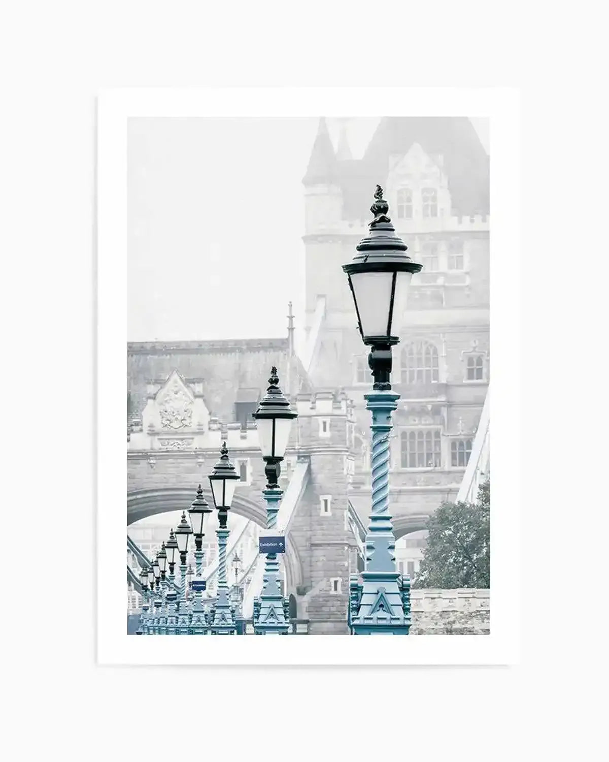 Framed photography art print of London's Tower Bridge on a misty day, with a row of blue lampposts in the foreground. The composition features the iconic bridge in soft grey tones, partially obscured by fog, with the ornate blue lampposts creating a leading line towards the distant towers. The mood is serene and atmospheric.