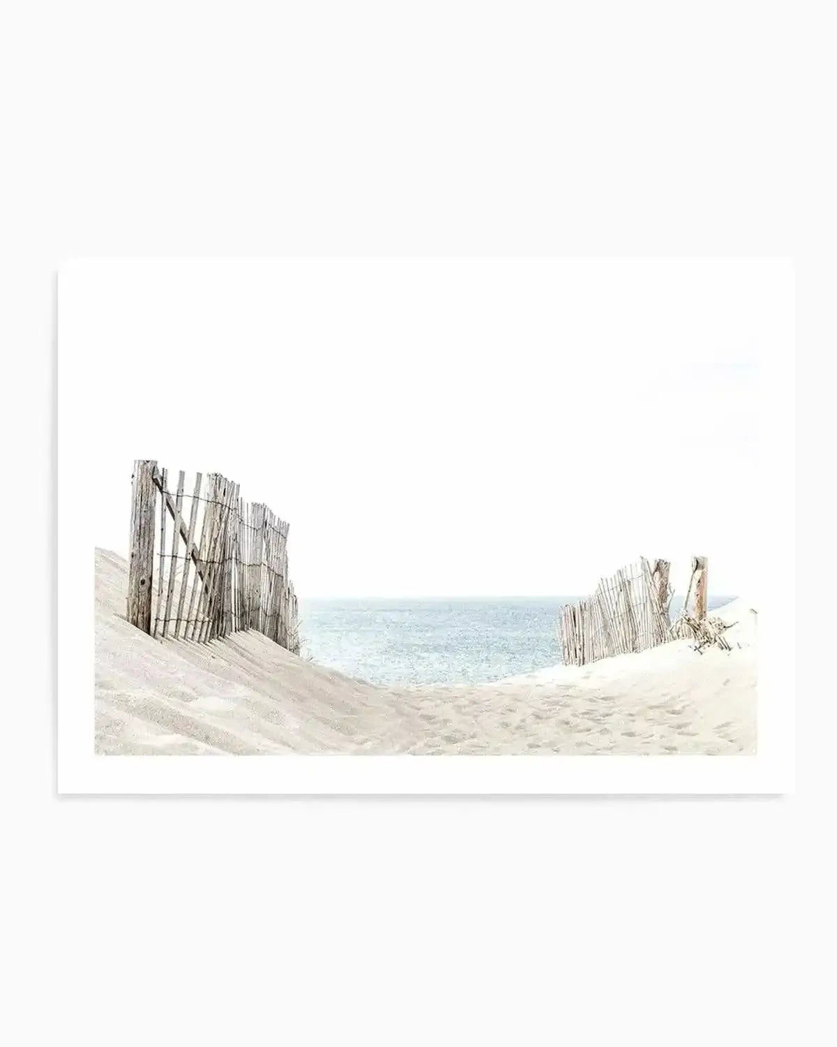 Framed photograph of a serene coastal beach scene with a path leading to the sea, printed on fine art paper. The composition features white sand dunes with weathered wooden fences on either side, opening up to a calm, light blue ocean under a bright white sky.