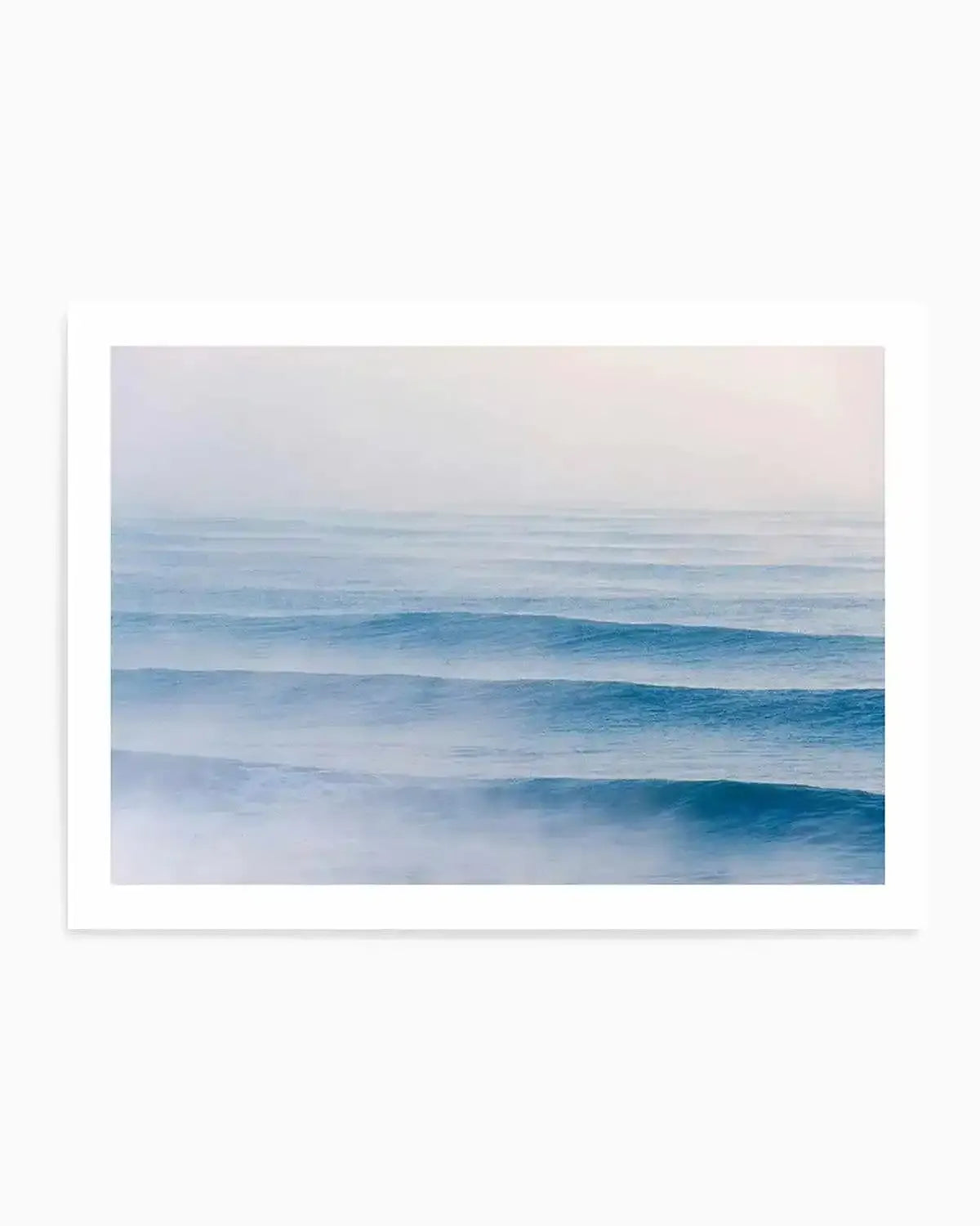 Framed photography art print of a serene ocean scene with gentle, parallel swell lines in varying shades of blue and white, with a soft, misty atmosphere. The composition features multiple horizontal waves rolling towards the viewer, with the foreground showing more detail and white foam, gradually fading into a hazy horizon.