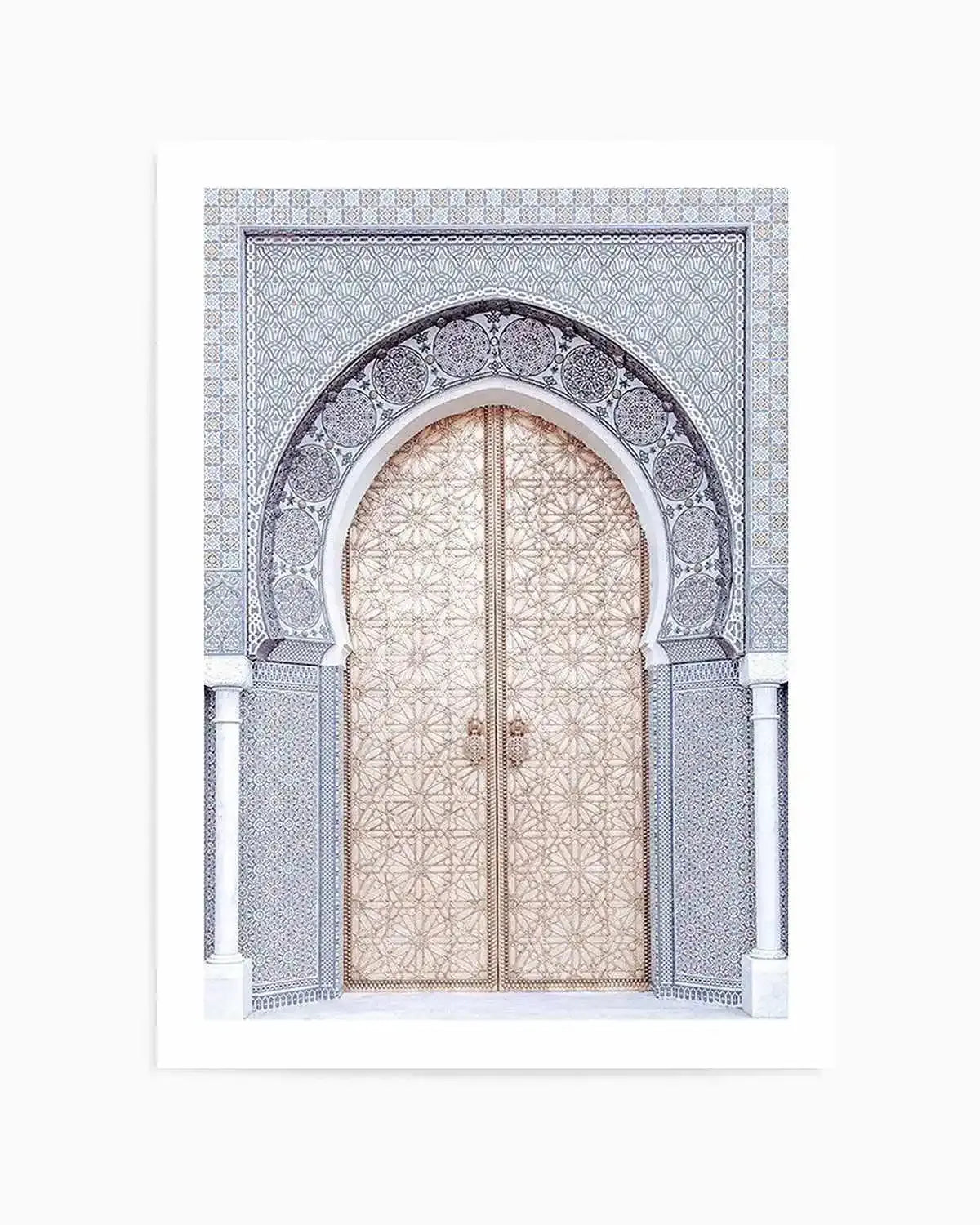 Product shot of an art print featuring a Moroccan archway and door in a light, neutral palette. The archway is intricately tiled in a repeating geometric pattern of light grey and white, with a darker grey border outlining the arch. The double doors beneath the arch are a light gold or champagne colour, also adorned with a detailed geometric pattern, and feature two small, ornate door handles. White columns flank either side of the archway, and the overall composition is symmetrical and elegant.