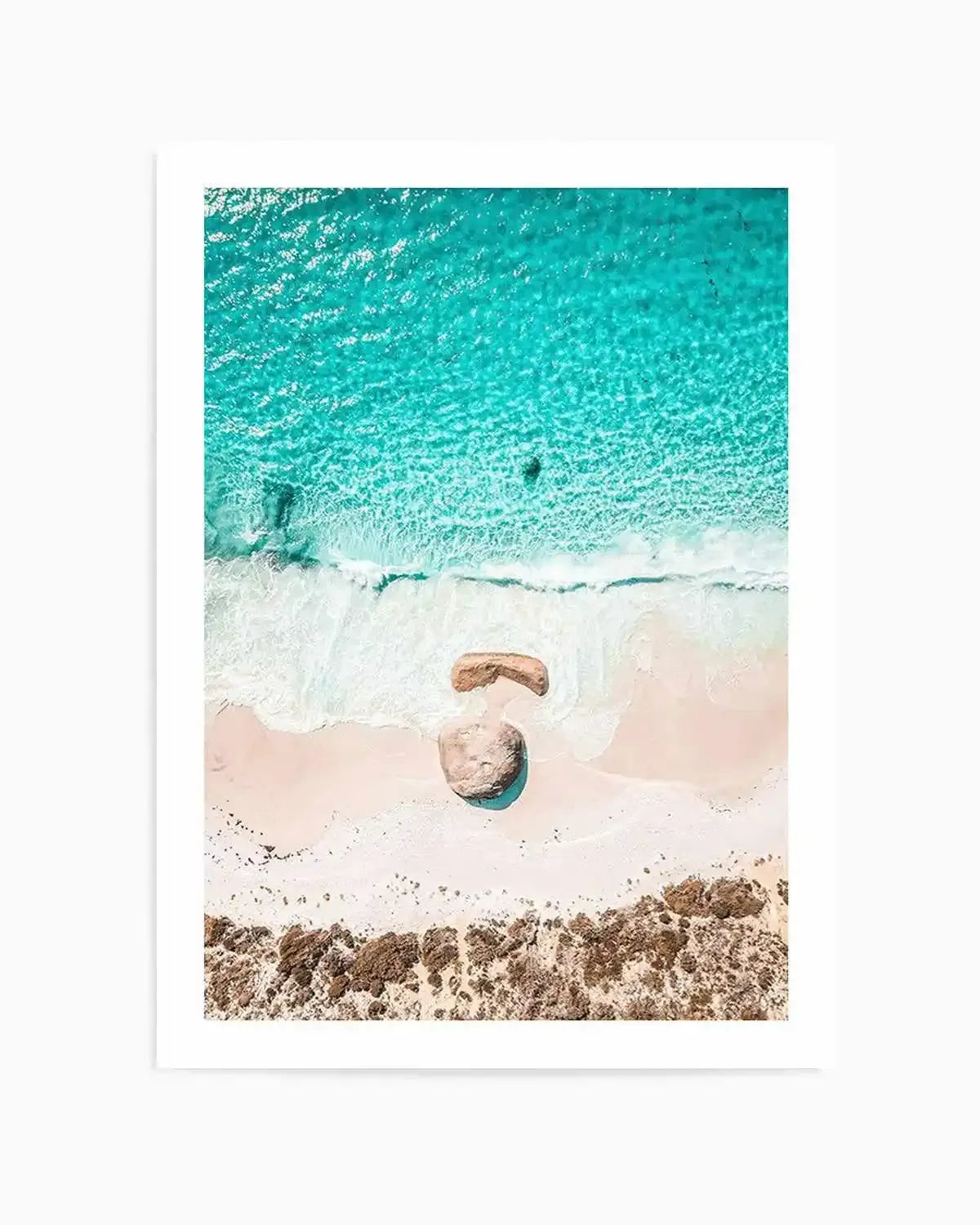 Aerial photography art print of a beach scene with vibrant turquoise ocean meeting a white sandy shore. The composition features two large rocks on the sand, one partially submerged in a shallow pool of water, and a line of brown coastal vegetation at the bottom.