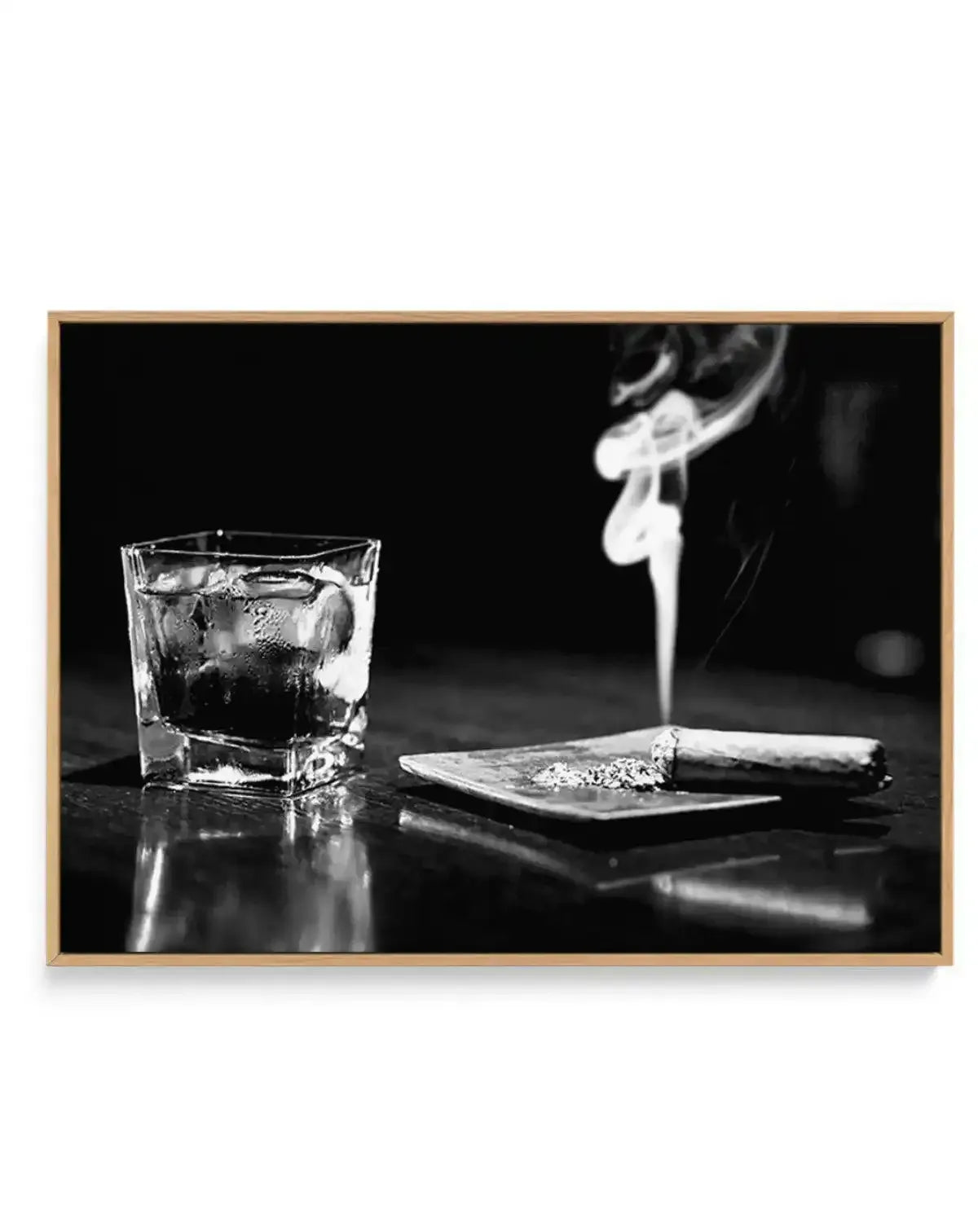 Black and white fine art photography displayed in a natural wood frame showing a crystal glass filled with dark liquor and ice on the left, a small white ceramic dish with a lit cigar in the center, and a hand holding a smoking cigar in the upper right against a dark background, capturing a moody, high-contrast composition with reflective surfaces.
