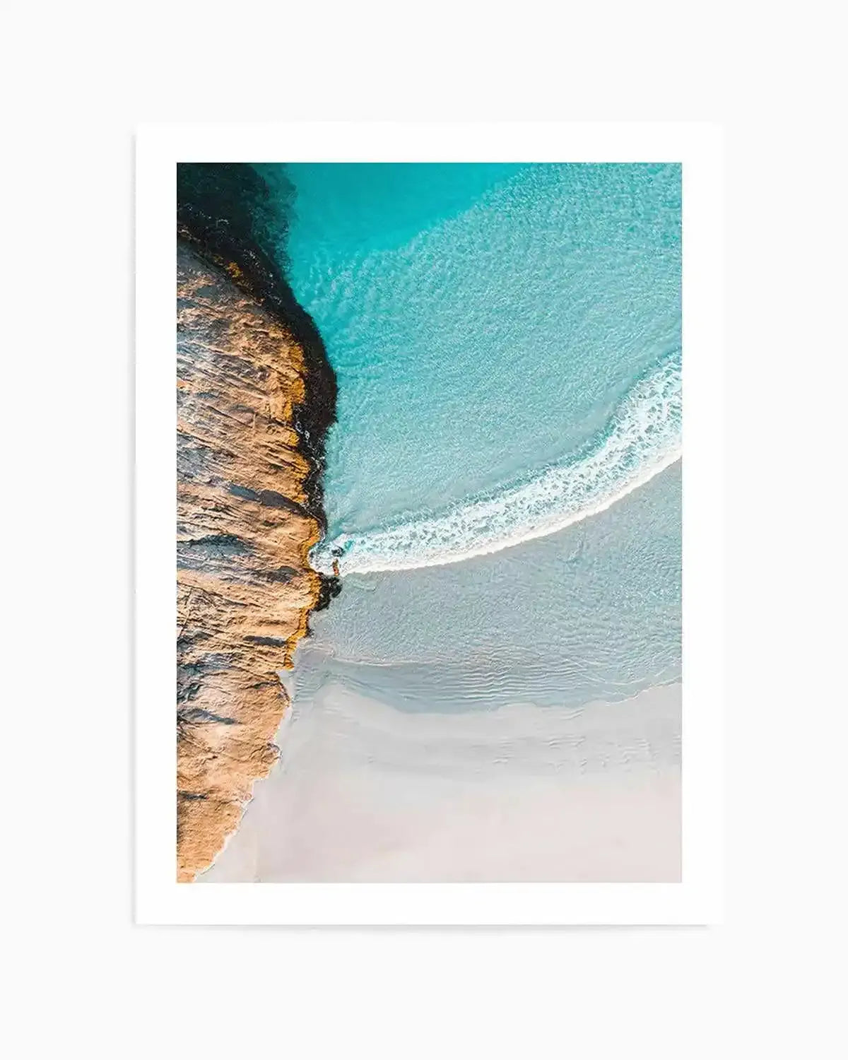 Aerial photography art print of a coastal scene featuring a rugged, textured rock formation in warm brown and orange tones on the left, meeting a vibrant turquoise ocean with clear, shallow water. A gentle white wave curves from the top right towards the bottom left, breaking onto a wide, light sandy beach.
