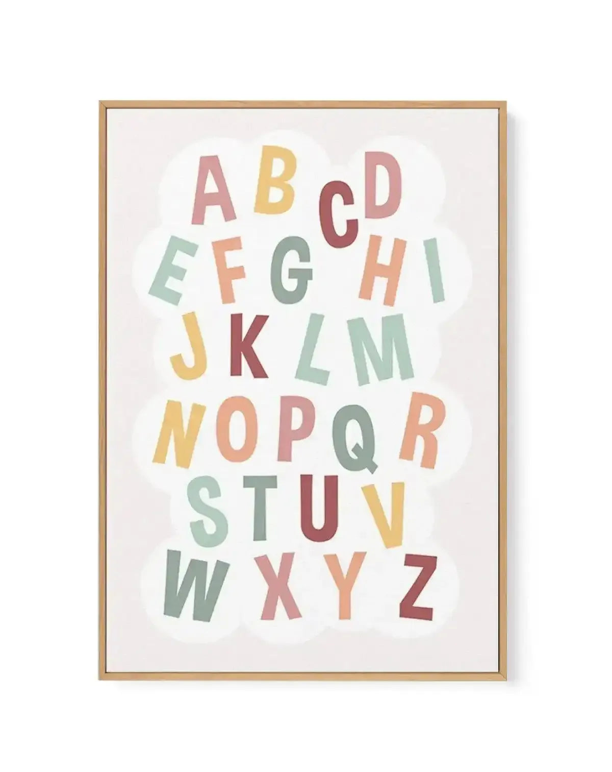 Framed canvas art print featuring the complete alphabet arranged in five rows against a soft white background with subtle cloud shapes. Letters in varying pastel colors including dusty rose, soft yellow, sage green, coral, burgundy, and muted blue. Natural wood frame with white border. Illustration style with playful, rounded letterforms suitable for children's spaces.