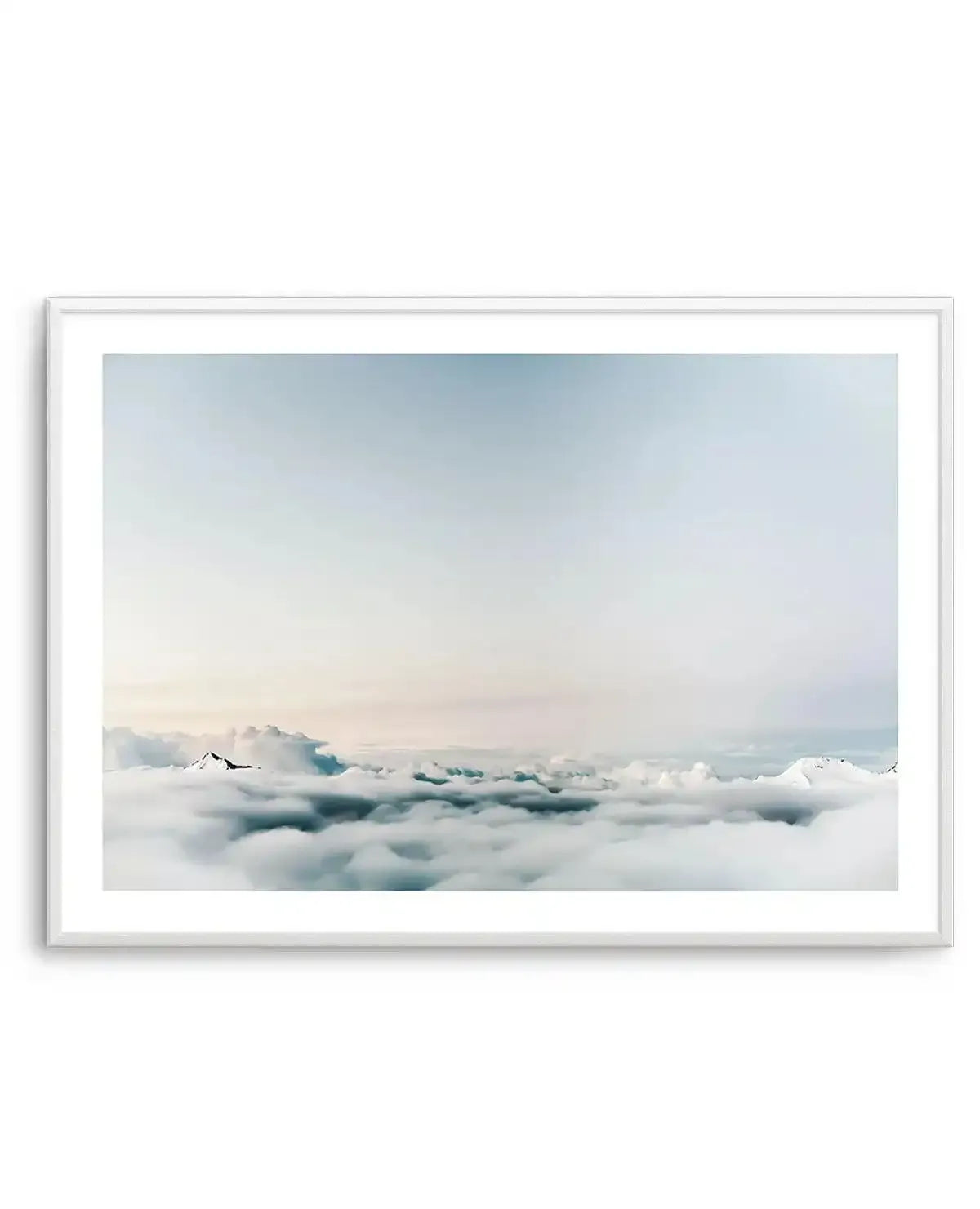 Framed photography art print featuring a serene aerial view of a vast cloudscape with a pale blue and soft pink sky above, and layers of white and muted teal clouds stretching to the horizon, with subtle peaks of distant mountains visible through the clouds. The print is displayed in a white frame with a white border.