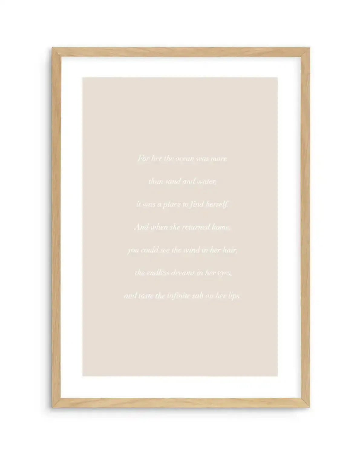 Art print featuring a poem in white serif font on a warm, pale beige background, displayed in a natural oak frame with white border. The poem reads: "For her the ocean was more than sand and water, it was a place to find herself. And when she returned home, you could see the wind in her hair, the endless dreams in her eyes, and taste the infinite salt on her lips."