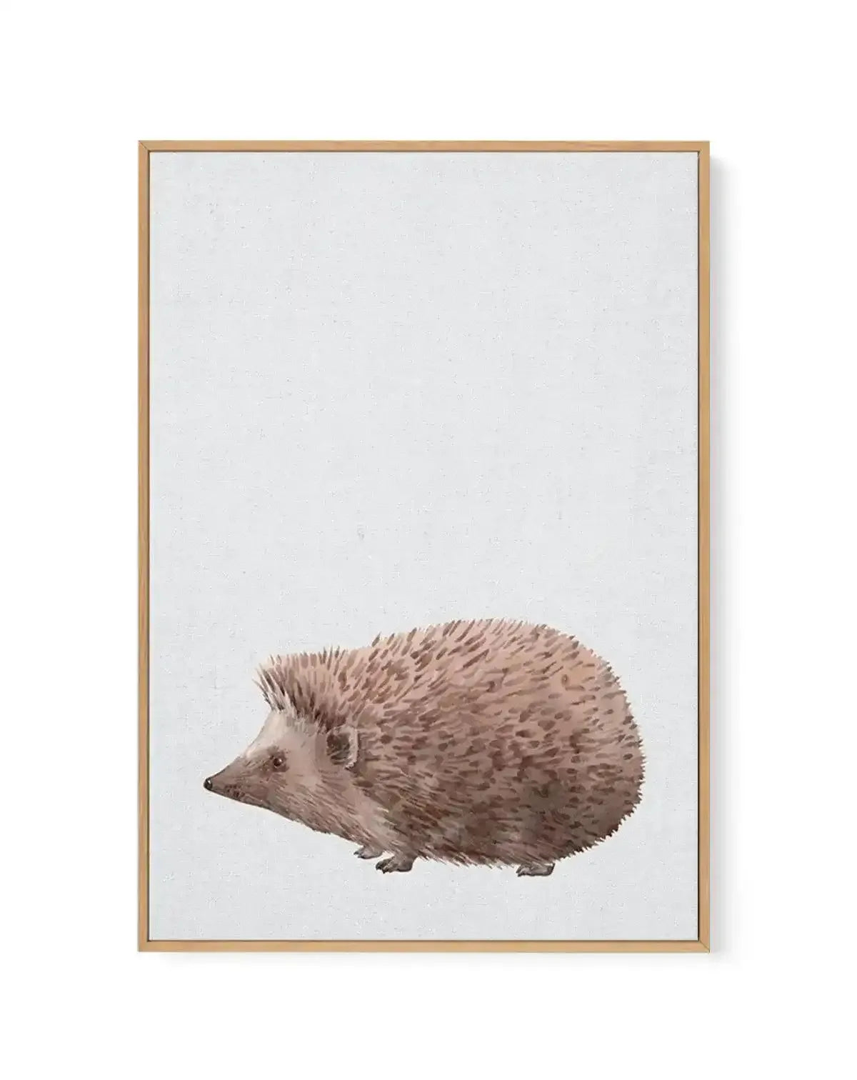 Framed canvas art print featuring a watercolor illustration of a hedgehog positioned in the lower center of a light gray background. The hedgehog is rendered in warm, muted tan and beige tones with detailed quill textures and a small dark eye. The artwork is displayed in a natural wood frame with a white border around the canvas, creating a minimalist, calm aesthetic.