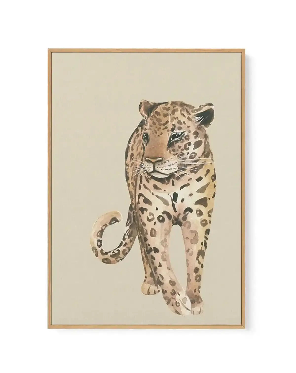Watercolor painting of a leopard walking forward against a cream background, framed in natural wood. The leopard features warm tan and beige tones with dark brown rosette spots and markings throughout its body, face, and curved tail. The artistic style uses soft watercolor washes creating a naturalistic yet painterly effect. The wooden frame has a simple, understated design with a white border around the canvas artwork.
