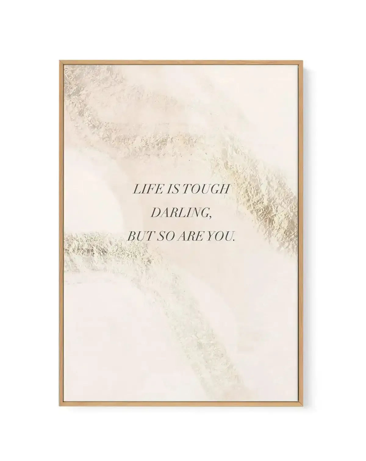 Framed canvas art print with natural wood frame displaying inspirational text "LIFE IS TOUGH DARLING, BUT SO ARE YOU" in serif italics centered on a cream background. Abstract brushstroke textures in soft gold and beige tones create diagonal sweeping marks across the upper right and lower left corners, giving a watercolor-like appearance. The overall composition has a minimalist, motivational aesthetic with neutral, warm tones.