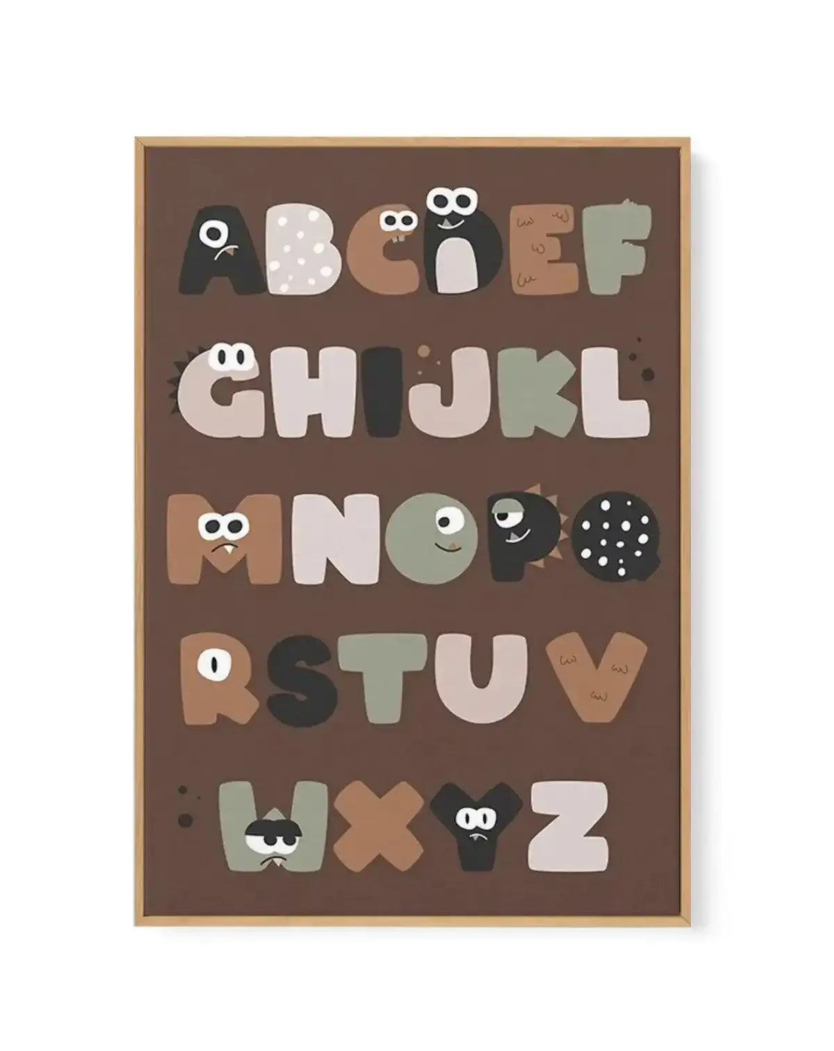 Framed canvas art print featuring the alphabet A to Z displayed vertically on a warm brown background. Each letter is illustrated as a friendly monster character in varying colors including cream, tan, sage green, black, and gray, with expressive eyes and playful details. The wooden frame is natural tan with a white border. Illustration style with a whimsical, child-friendly design.