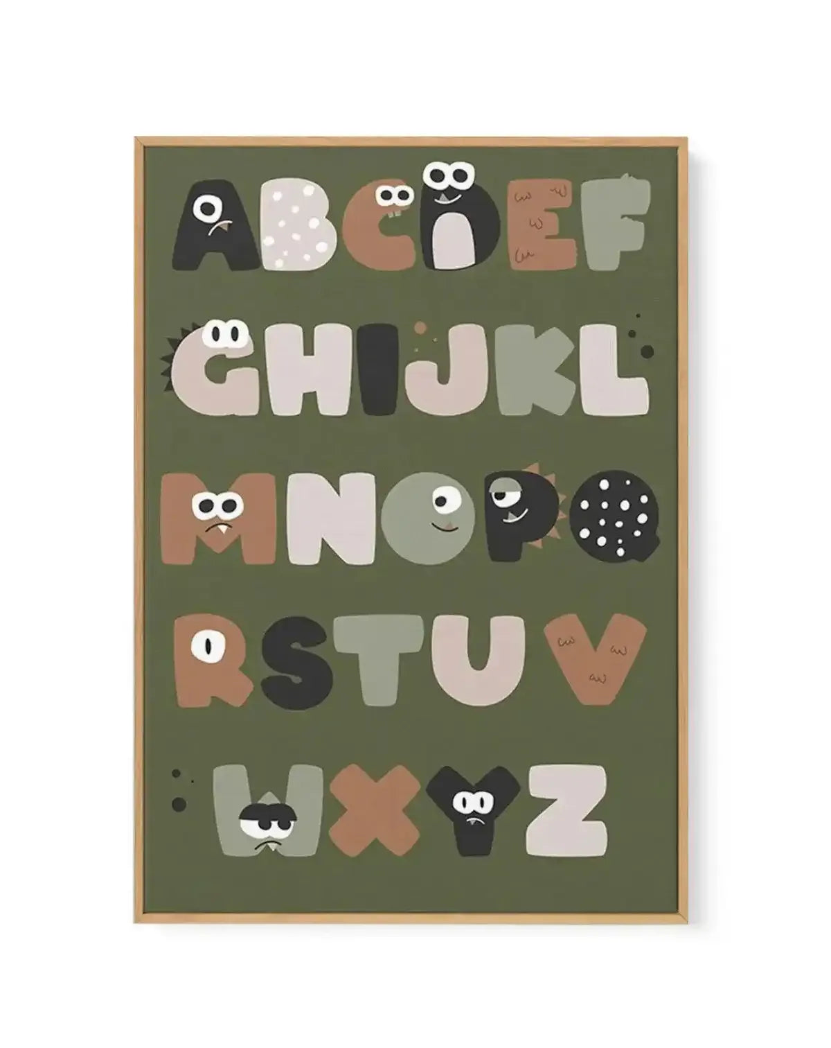 Framed canvas art print featuring an illustrated alphabet on a sage green background. Each letter from A to Z is designed as a friendly monster character with googly eyes and simple facial features in shades of cream, tan, brown, and black. The letters are arranged in five rows across the canvas. The print is mounted in a natural wood frame with a white border.