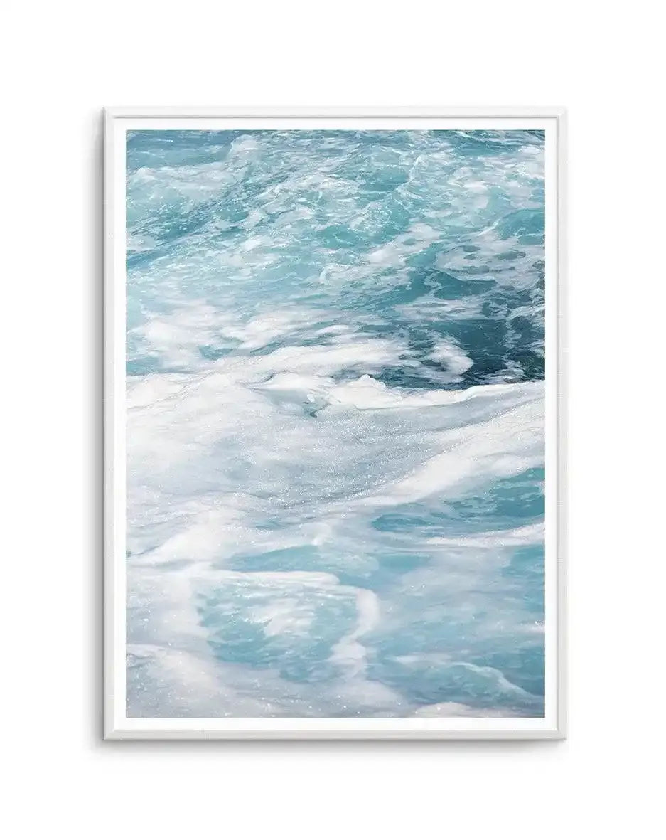 Framed art print featuring a photograph of ocean waves and sandy beach. The composition shows turquoise and teal waves with white foamy crests in the upper portion, transitioning to wet sand with gentle waves lapping at the shore in the foreground. The palette includes soft whites, pale aqua, and deeper ocean blue-greens, creating a serene coastal scene. The photograph has a soft, natural light quality with visible sparkle on the water. The artwork is displayed in a white wooden frame with a white border.