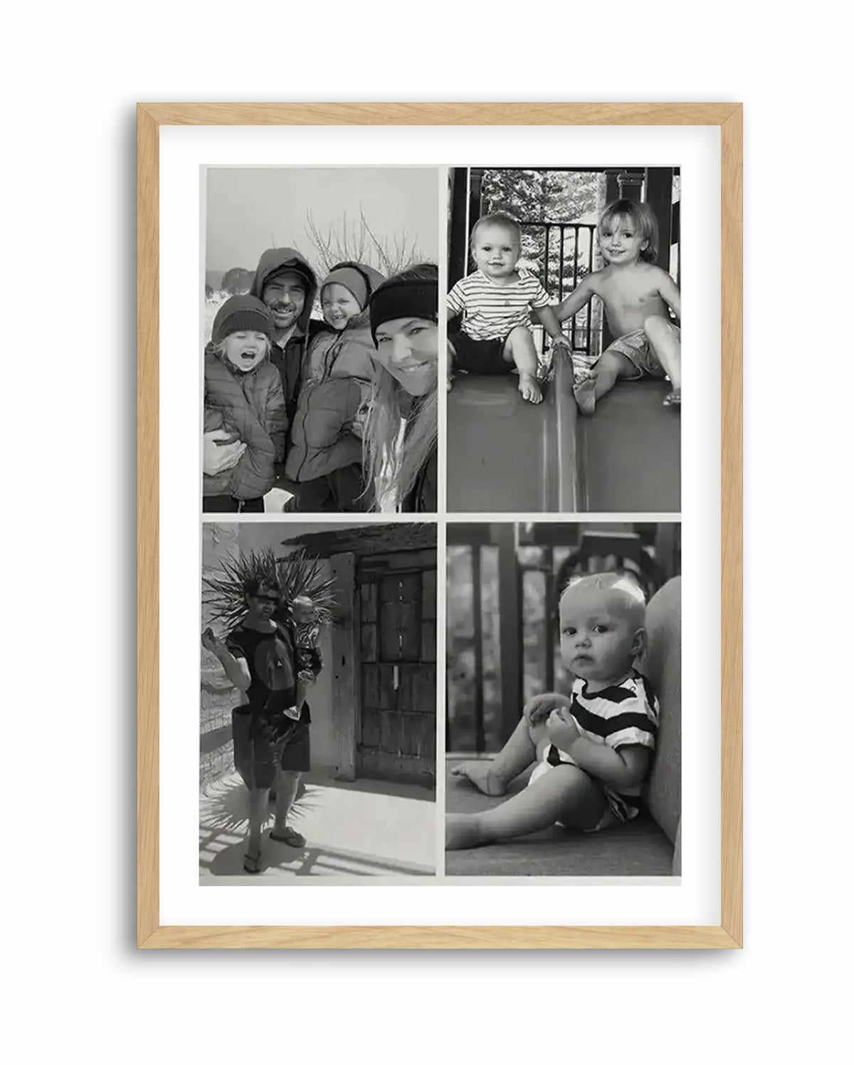 Framed black and white photography art print featuring four individual family photos arranged in a grid, displayed in a natural oak frame with white border. The top left photo shows a family of four in winter clothing, smiling. The top right photo shows two young children, one shirtless, sitting on a playground slide. The bottom left photo shows a man holding a baby outdoors. The bottom right photo shows a baby sitting on a cushion.