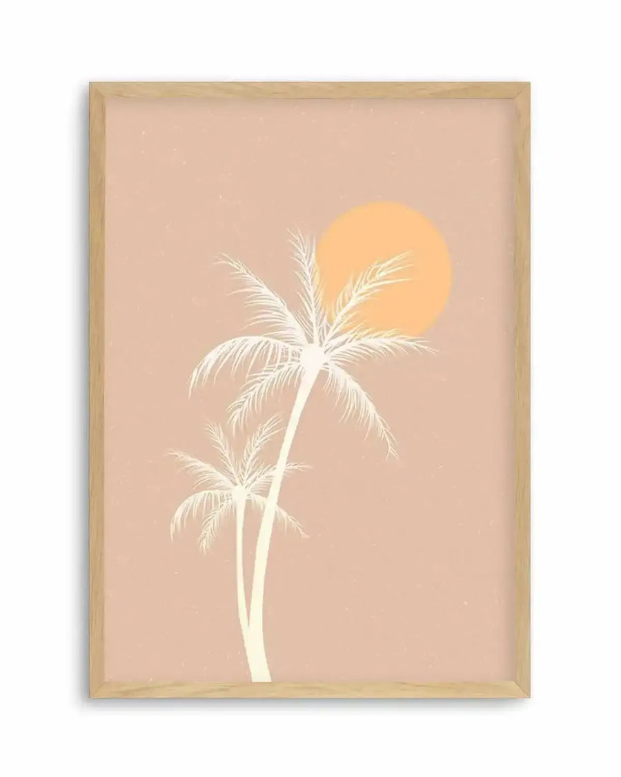 Art print featuring two stylized palm trees in a creamy white silhouette against a dusty rose background, with a large, warm orange sun partially visible behind the taller palm tree. The print is displayed in a natural oak frame with a white border.