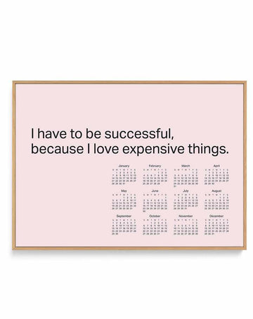 Blush pink calendar poster with bold black motivational quote and 12-month grid, in a natural wood frame