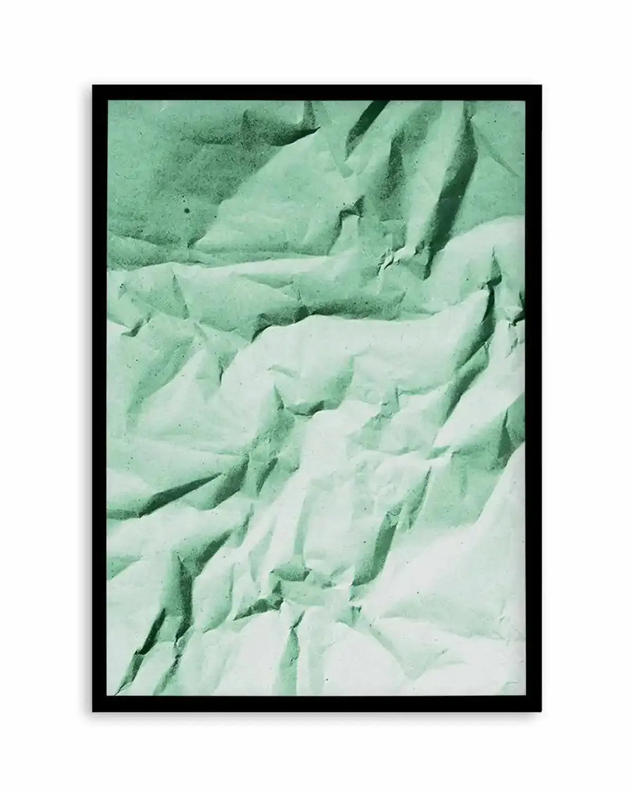 Abstract art print featuring a crumpled paper texture in varying shades of muted sage green and pale mint, creating deep shadows and highlights across the surface, displayed in a black frame with a white border.