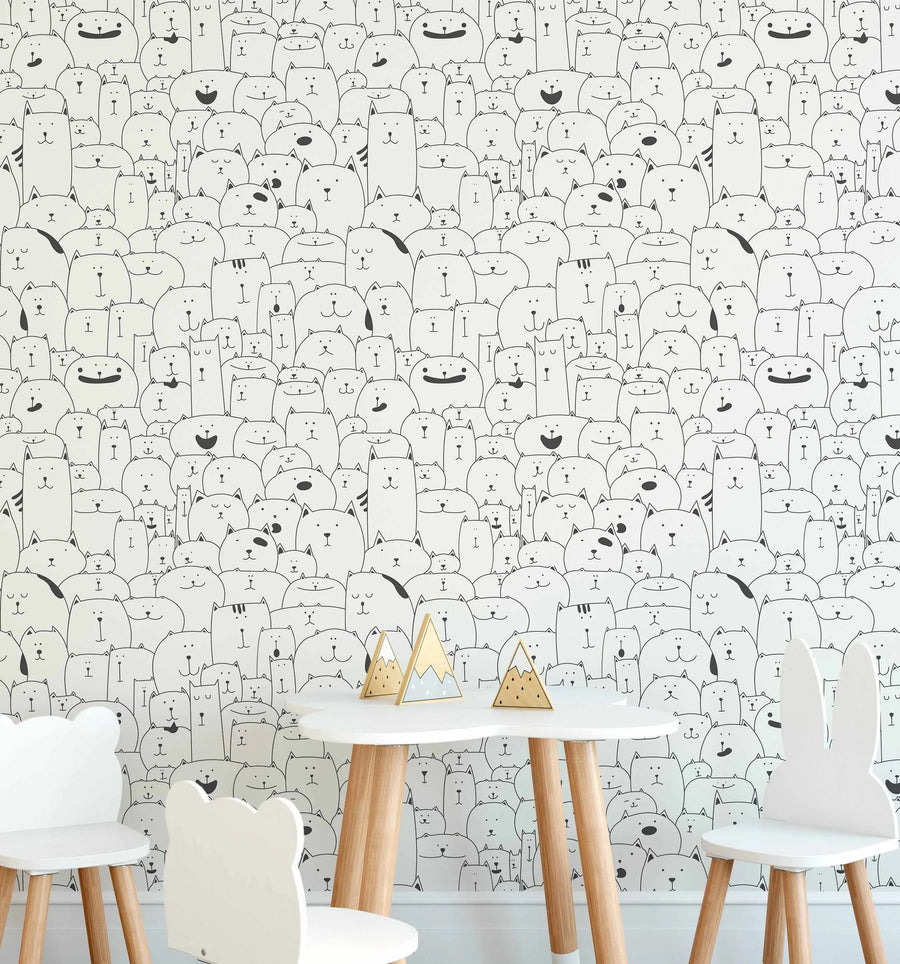 Lifestyle shot featuring a children's play area with a white table and chairs against a wallpapered wall. The wallpaper features a repeating pattern of hand-drawn cats in black outline on a white background, with various expressions and shapes. The table has three small wooden mountain-shaped decorations.