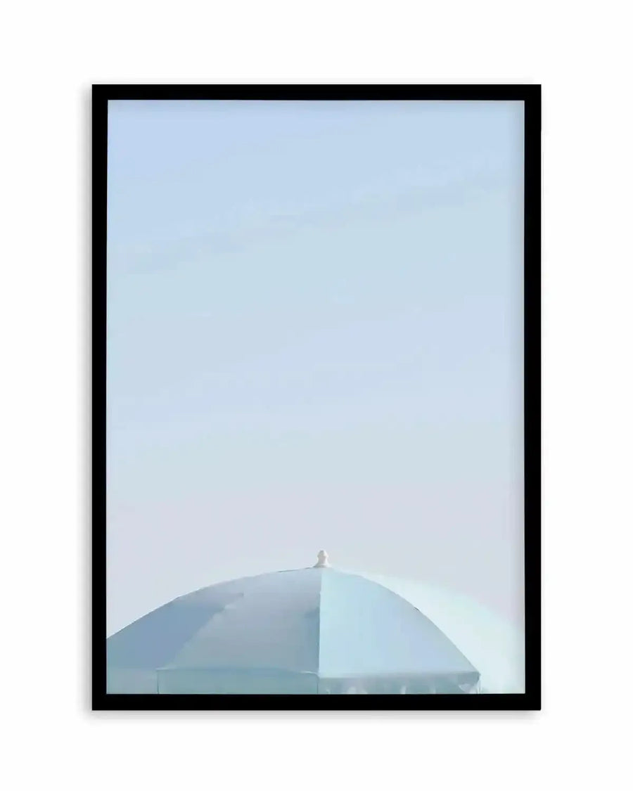 Framed art print featuring a minimalist photograph of the top of a light aqua blue parasol against a pale blue sky, with a black frame and white border.