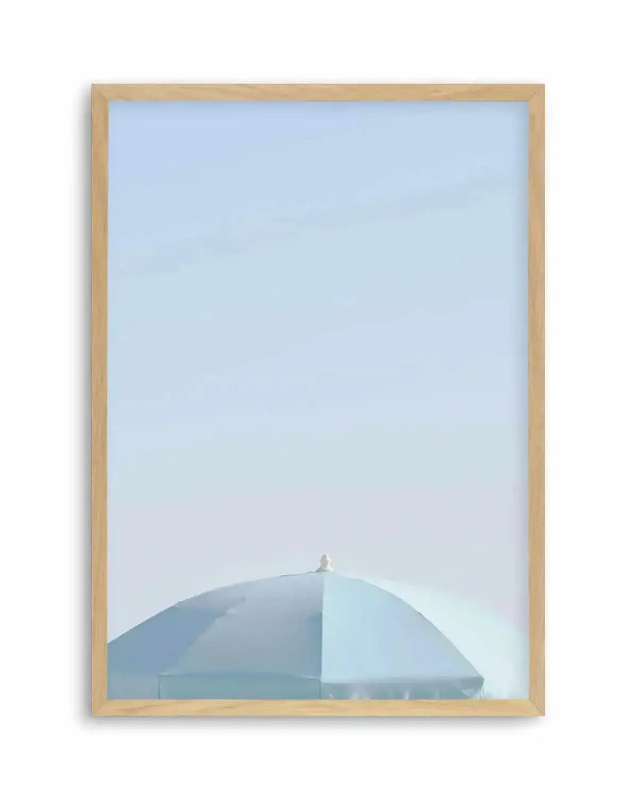 Framed photography art print of an aqua parasol against a pale blue sky, with a natural wood frame and white border. The parasol is a muted aqua blue, with a white finial at its peak, and occupies the lower third of the composition.