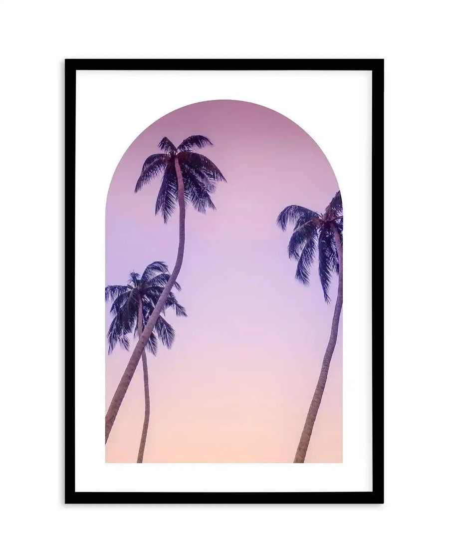 Framed photography art print featuring three palm trees against a gradient sky, displayed in a black frame with white border. The sky transitions from a soft purple at the top to a warm peach at the bottom, creating a serene, tropical mood. The palm trees are silhouetted, with dark fronds and slender trunks, two leaning towards the left and one on the right.
