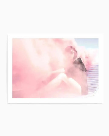 "Art print featuring a hazy, dreamlike photograph of a person partially obscured by dense, billowy pink smoke. The person is seated, with visible legs and torso, and their head is turned slightly to the side, looking into the smoke. The background shows hints of a light blue sky and what appears to be a white, ribbed surface on the right, possibly a wall or structure. The overall mood is soft and ethereal, with a focus on the vibrant pink smoke."