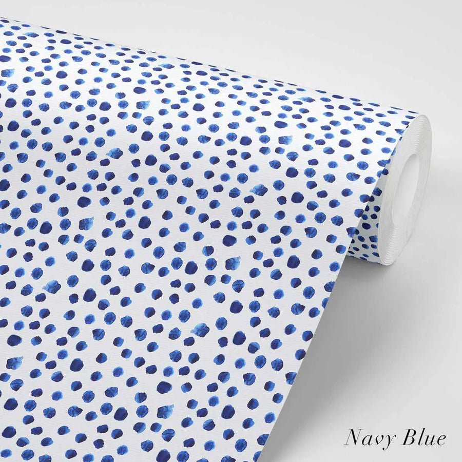Peel and stick wallpaper featuring a repeating pattern of hand-painted irregular dots in various shades of navy blue on a crisp white background. The dots have a loose, organic watercolor quality with visible brushstroke texture. The wallpaper is shown rolled up, with a section unfurled to display the pattern.