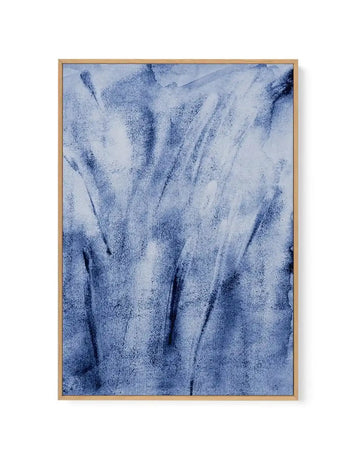 Framed canvas art print titled Belvedere I featuring an abstract composition in shades of blue and white. The artwork displays vertical brushstrokes and layered textures creating a watercolor-like effect, with darker navy streaks flowing downward against a lighter periwinkle and cream background. The piece is displayed in a natural wood frame with a white border, mounted on a white wall.