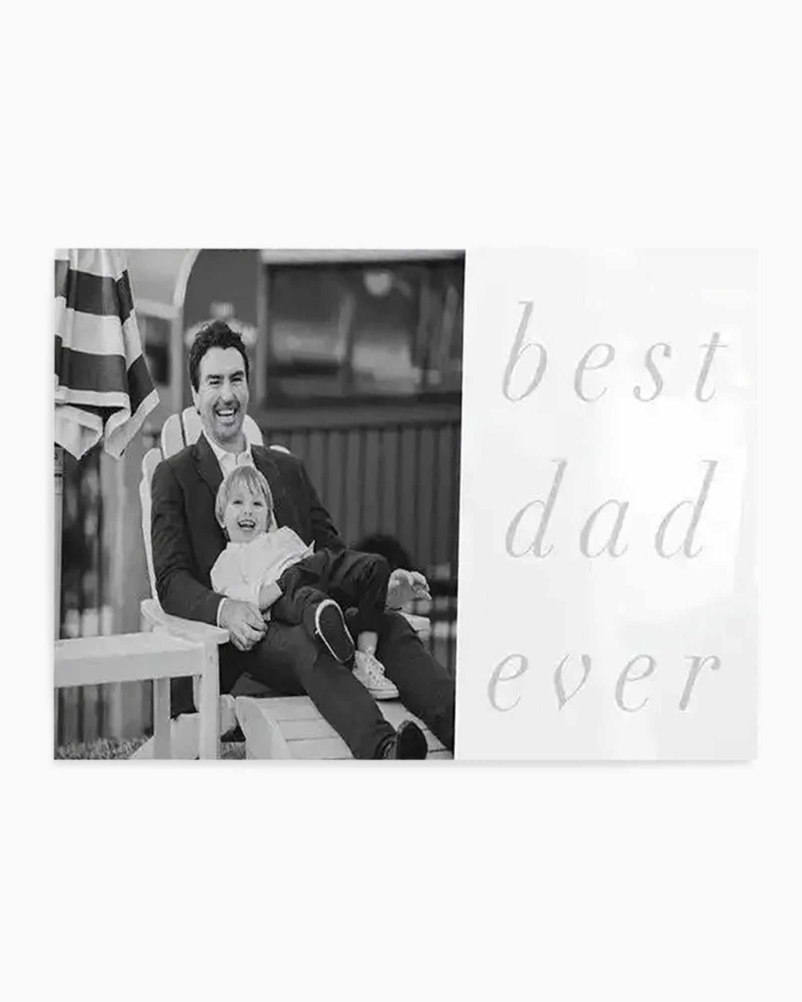 Black and white art print featuring a custom photo design. Left side displays a black and white photograph of a smiling man holding a young child, both seated outdoors with a striped flag visible in the background. Right side shows light gray serif text reading "best dad ever" in a thin, elegant typeface. The overall composition is minimalist on a white background, combining photography with typography for a keepsake-style design.