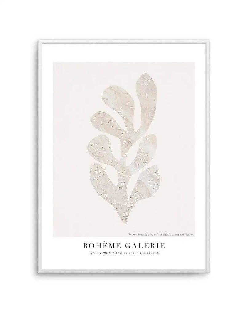 Framed art print featuring an abstract, organic shape resembling a stylized leaf or coral in a light, textured stone or concrete finish against a soft, off-white background, displayed in a white frame with white border. The texture of the shape includes subtle variations in light beige and grey tones with small, dark flecks. Text at the bottom reads "BOHÈME GALERIE" and "AIX EN PROVENCE 43.5297° N, 5.4474° E" with a smaller line above saying "la vie dans la pierre" | A life in stone exhibition".