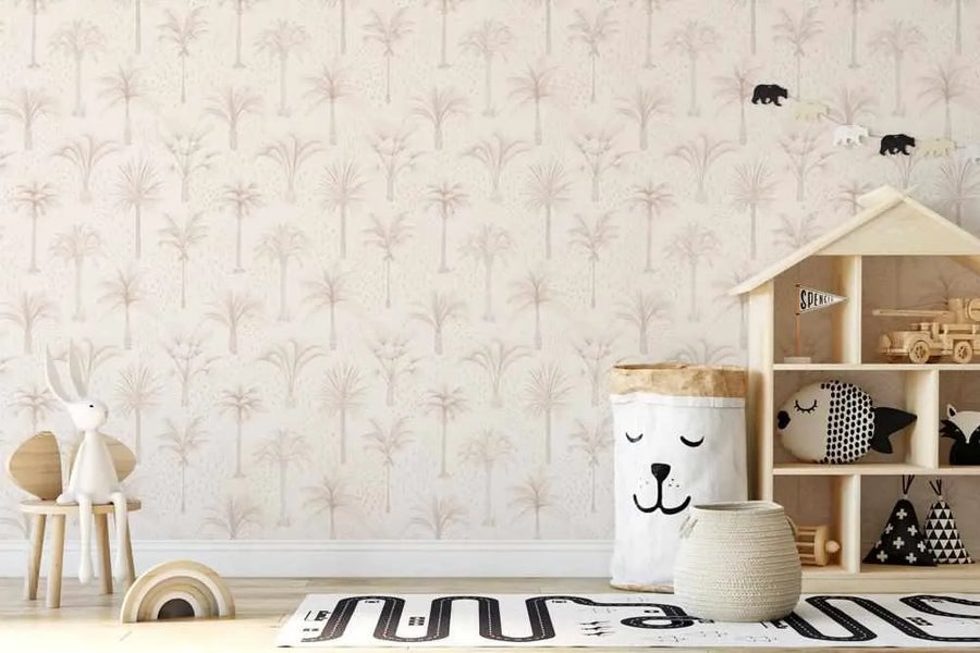 Nursery:
"Bohemian Palms Wallpaper featuring a repeating pattern of hand-painted palm trees in muted beige and dusty rose on a cream background, with subtle speckle texture. The wallpaper is displayed in a child's room with a wooden dollhouse shelf, a white bear-shaped storage bag, a white bunny toy on a wooden chair, a rainbow stacking toy, and a black and white road-patterned rug."