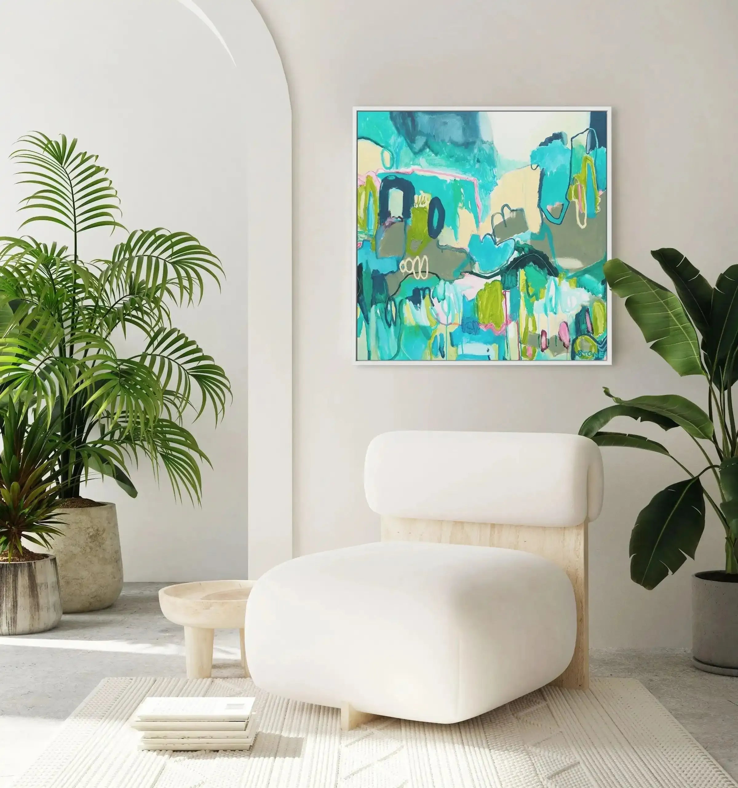 Lifestyle shot of a minimalist living room featuring a framed abstract canvas print above a white upholstered chair. The print, titled "Bondi Blues," showcases an abstract composition of vibrant turquoise, teal, lime green, and pale yellow brushstrokes with accents of soft pink and grey, framed in white. The room includes two large potted plants with green foliage, a small wooden side table, and a textured cream rug.