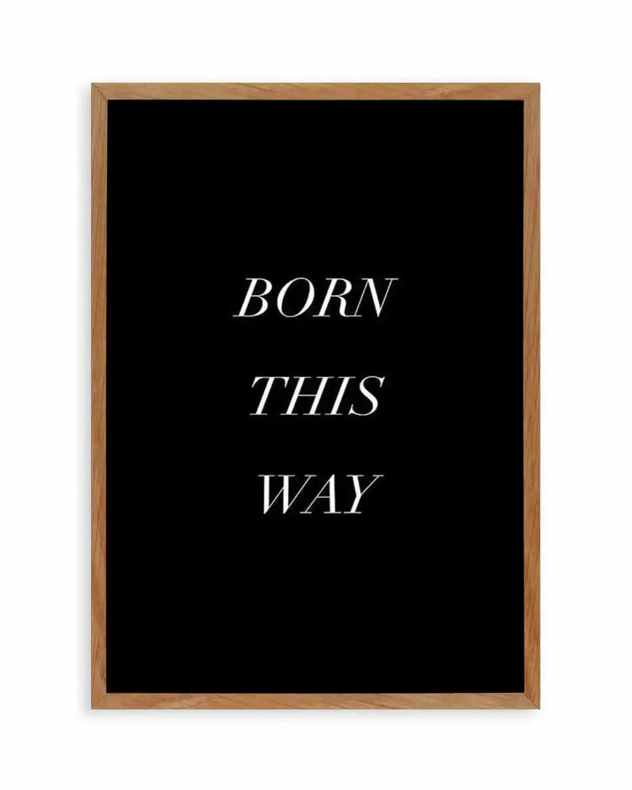 "Typographic art print featuring the words 'BORN THIS WAY' in three lines of white serif font on a solid black background, displayed in a natural oak frame with white border."