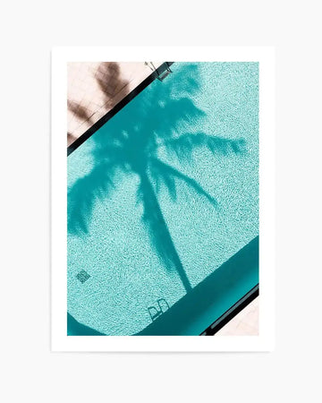 "Photography art print of a swimming pool from an aerial perspective, featuring a large shadow of a palm tree cast across the turquoise water. The water has a rippled texture, and the pool edge is visible with a ladder in the bottom right corner. The surrounding pool deck is a light, textured tile."