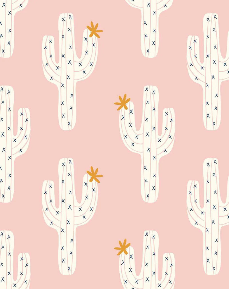 Peel and stick wallpaper featuring a repeating pattern of hand-drawn saguaro cacti in off-white with small navy blue 'x' marks representing needles, on a soft blush pink background. Some cacti have a small, five-petal orange flower blooming from their arms or tops. The illustration style is simple and playful.