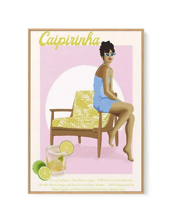 Framed canvas art print featuring a retro-style illustration of a woman in a light blue dress and white cat-eye sunglasses, sitting on a yellow and green patterned chair. The background is a soft pink with a large white circle. In the foreground, a glass of caipirinha with lime slices and whole limes is shown, along with the recipe text in yellow. The print is displayed in a natural wood frame with a white border.