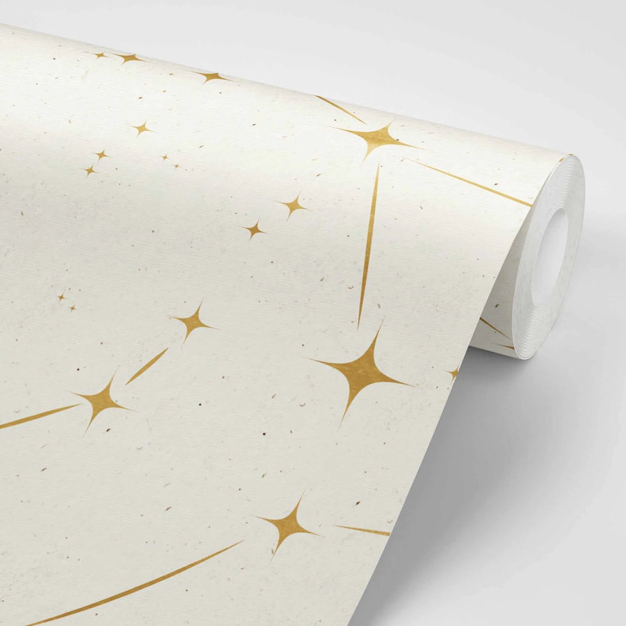 "Peel and stick wallpaper featuring a repeating pattern of gold celestial stars with radiating lines on a textured cream background. The stars have a metallic sheen and vary in size, creating a scattered, constellation-like design."