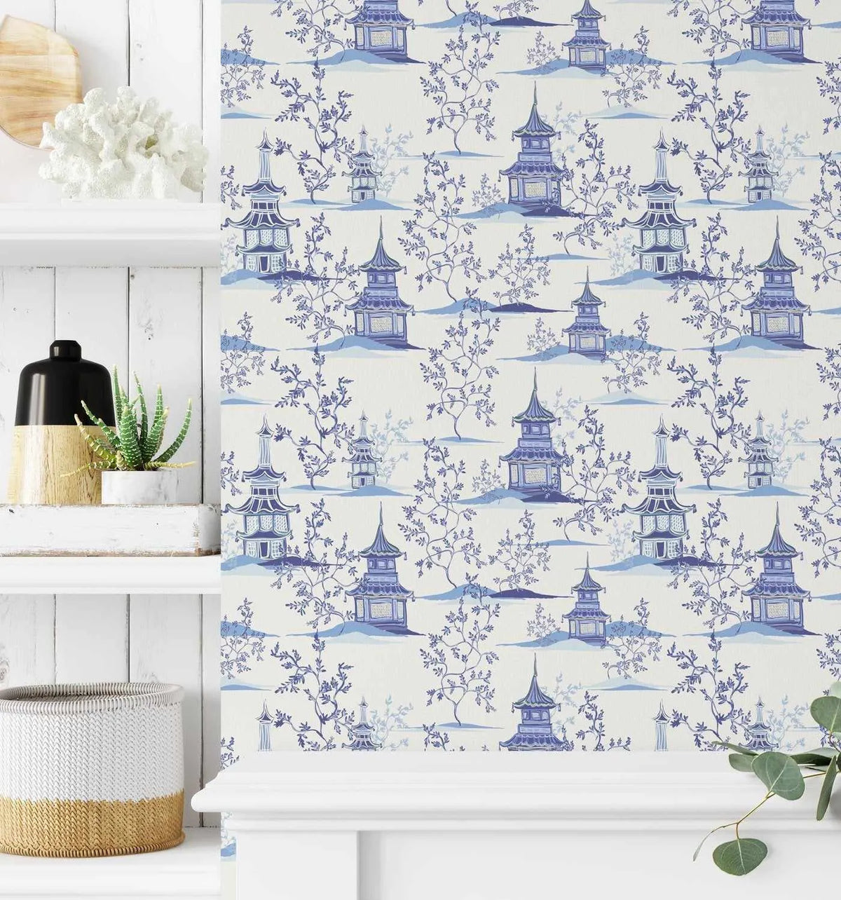 Peel and stick wallpaper featuring a repeating pattern of hand-painted blue and white chinoiserie pagodas and winding trees with delicate branches on a light cream background. The design has a watercolour quality with varying shades of blue, from deep indigo to pale sky blue, creating depth and texture.