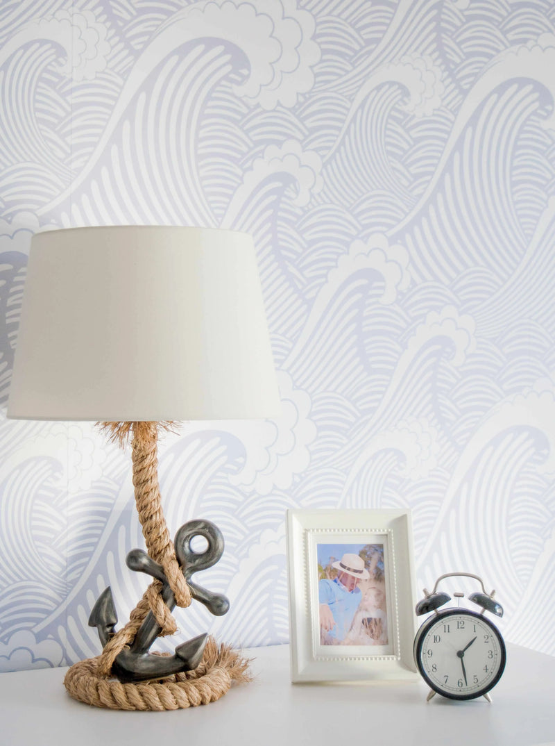 "Peel and stick wallpaper featuring a repeating pattern of stylized ocean waves in a soft, muted periwinkle blue against a clean white background. The design includes large, curling waves with parallel lines indicating movement, interspersed with smaller, cloud-like foam details."