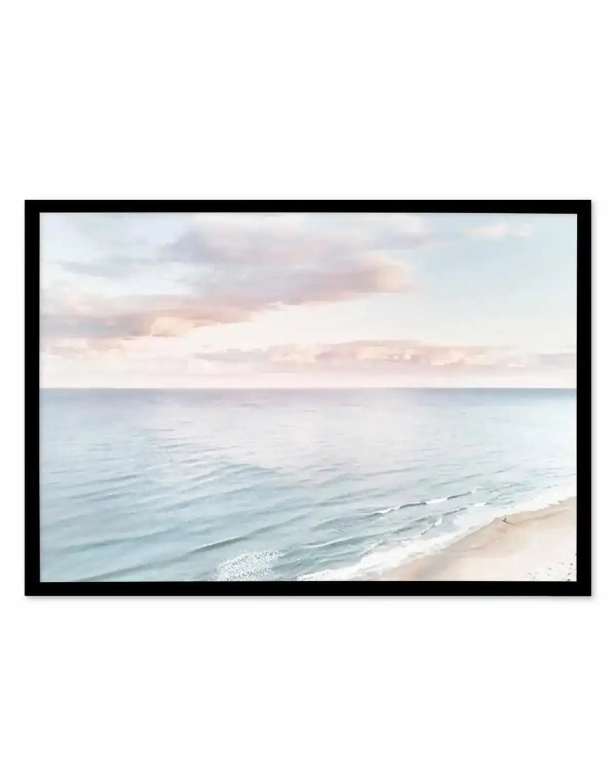 Pastel coastal seascape print in thin black frame — soft blue ocean and sandy shore