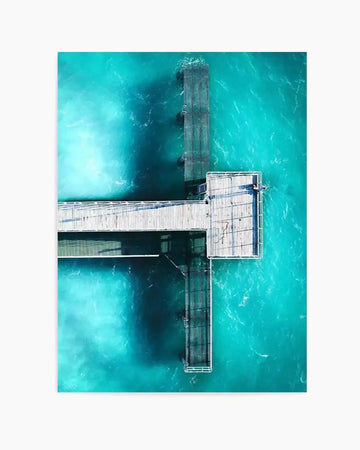 Aerial photography art print of Coogee Jetty in Western Australia, featuring a wooden pier extending into vibrant turquoise ocean water. The pier forms a T-shape, with a long walkway leading to a wider platform, casting dark shadows on the clear water below. The water shows subtle ripples and variations in depth, with lighter areas near the surface and darker tones where the pier's structure is visible beneath.