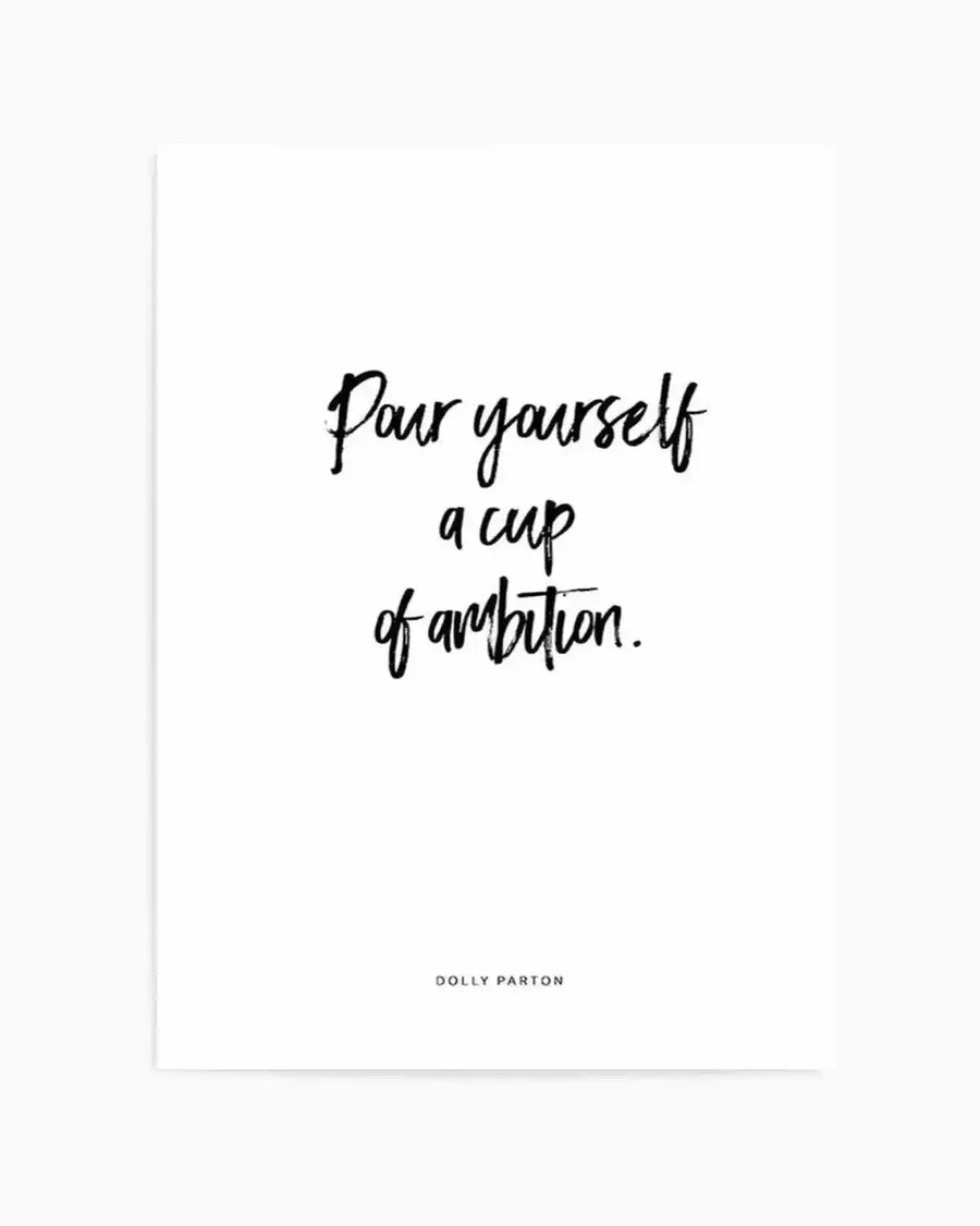 Art print featuring the quote "Pour yourself a cup of ambition." in a handwritten, brushstroke-style black font on a clean white background, with "DOLLY PARTON" in a smaller, sans-serif black font at the bottom.
