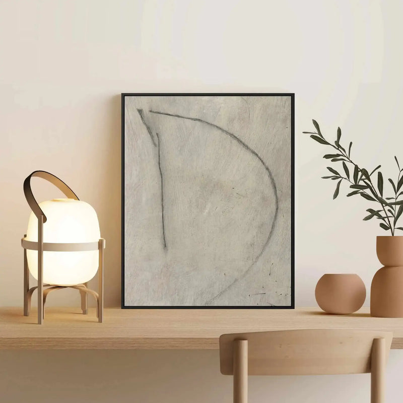 Framed canvas art print featuring a minimalist line drawing of the letter 'D' in charcoal gray on a textured beige background. The black frame is displayed on a light wooden shelf alongside a glowing portable lamp with brown leather handle, terracotta ceramic vessels, and fresh green foliage in matching earth-tone planters. The overall composition demonstrates a warm, neutral aesthetic with natural materials and soft lighting.