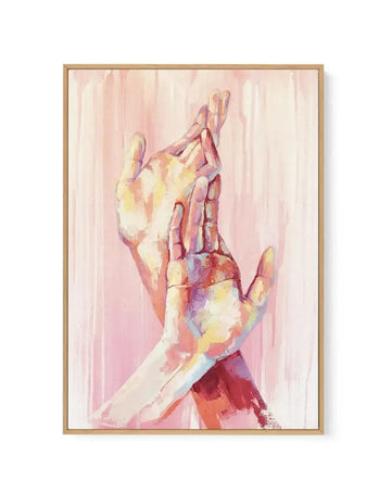 Framed canvas art print featuring an abstract watercolor painting of two hands reaching upward against a soft pink background. The hands are rendered in loose, flowing brushstrokes with warm tones of cream, yellow, coral, and deep rose, creating an ethereal quality. The composition emphasizes gesture and movement, with vertical streaks of paint suggesting emotion and freedom. Natural wood frame with white border surrounding the artwork.