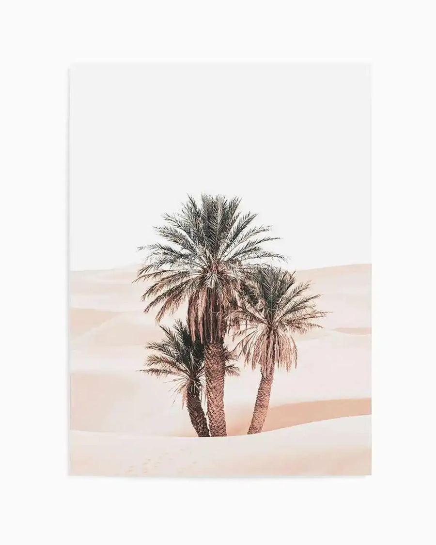 Photography art print featuring three palm trees in a desert landscape with soft, muted tones. The composition shows the palm trees standing in rolling sand dunes under a bright, almost white sky. The sand is a pale, dusty rose colour with subtle shadows defining the curves of the dunes. The palm fronds are a muted green-grey, and the trunks are a warm brown, blending harmoniously with the desert colours.