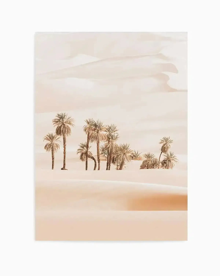 "Photography art print featuring a serene desert landscape with soft, muted tones. The composition shows a cluster of palm trees with feathery fronds in the middle ground, surrounded by gently rolling sand dunes in varying shades of pale peach and cream. The sky is a soft, hazy beige, blending seamlessly with the distant dunes, creating a tranquil and minimalist scene."