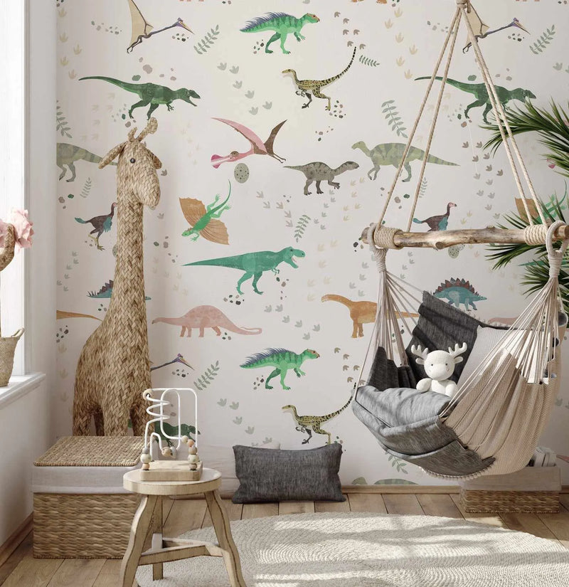 Nursery:
"Peel and stick wallpaper featuring a repeating pattern of various dinosaurs and prehistoric creatures in muted green, brown, pink, and blue tones on a soft white background, with scattered leaves and footprints. The wallpaper is displayed in a child's room with a large woven giraffe toy, a wooden stool with a bead maze, and a hanging hammock chair with a white stuffed reindeer."