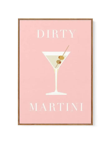 Framed canvas art print featuring a minimalist illustration of a martini cocktail on a blush pink background. The drink is rendered in cream and pale yellow tones with two olive garnishes on a cocktail pick. White serif typography reads "DIRTY" at the top and "MARTINI" at the bottom. The canvas is set in a warm medium-brown wooden frame with a white border.